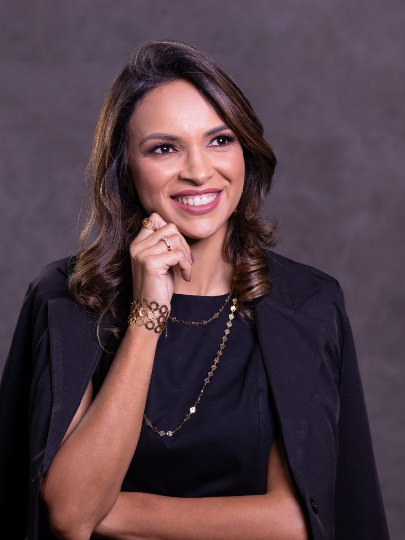 Retrato de Arienny Mergulhão de blazer preto, sorrindo, com a mão no queixo