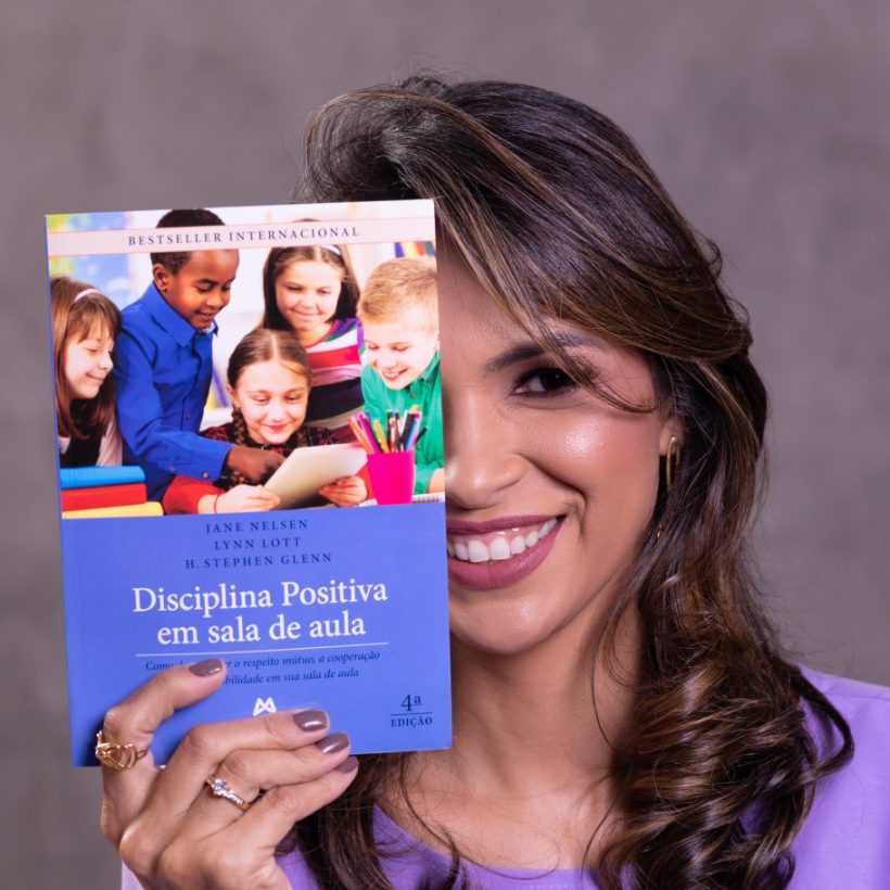 Arienny Mergulhão sorrindo por trás do livro Disciplina Positiva em sala de aula